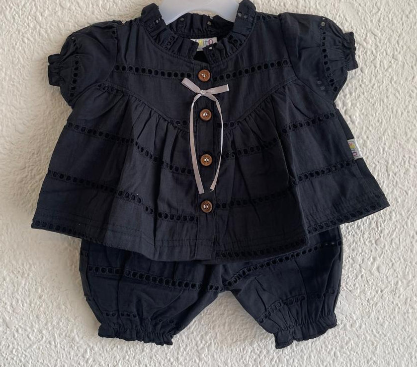 A baby girl's two-piece outfit consisting of a dark navy blue eyelet lace top with a ruffled collar, button front, and matching eyelet bloomers, hanging on a white hanger against a textured off-white wall.